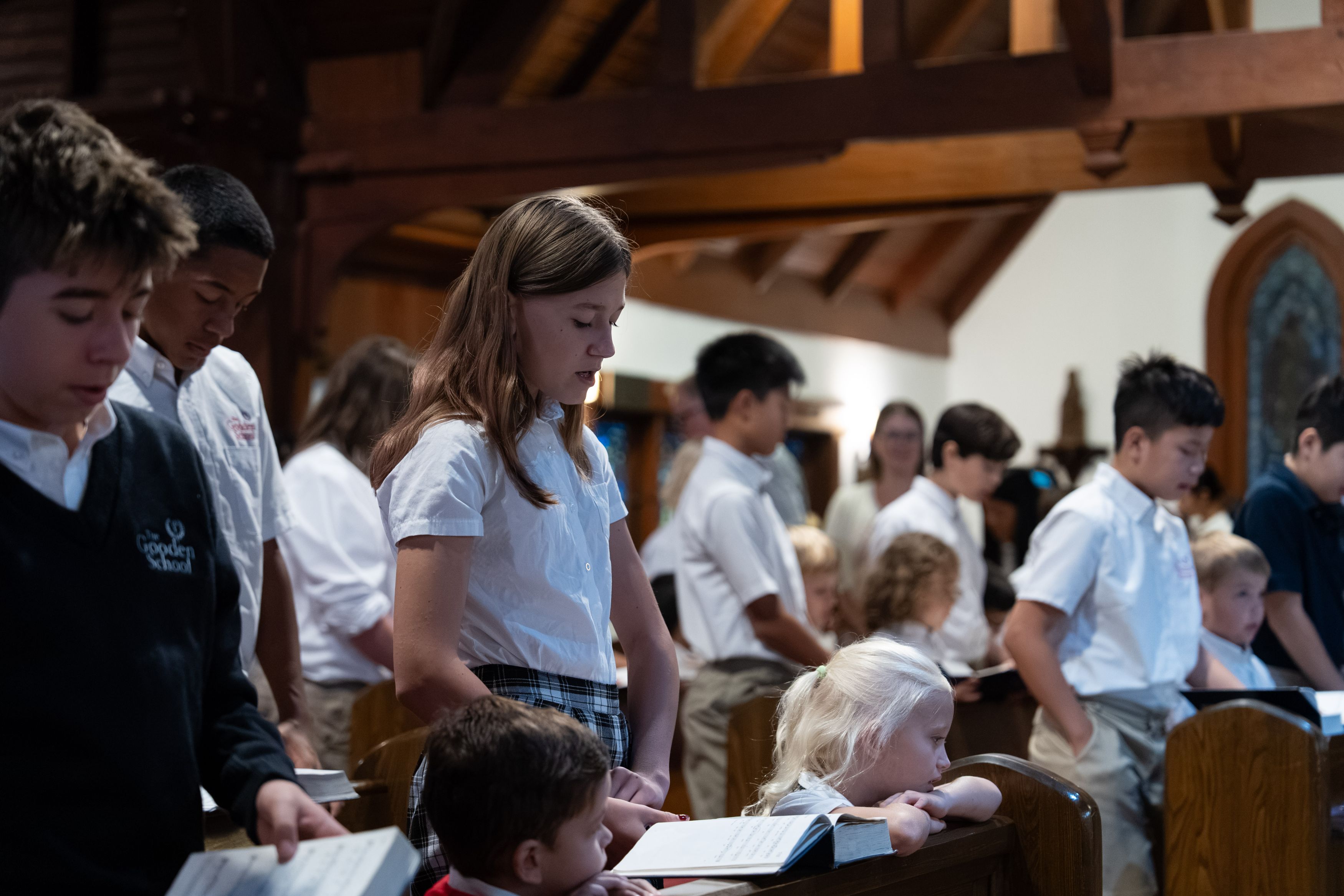 Students from The Gooden School stand in a church, singing from hymnals during a service.