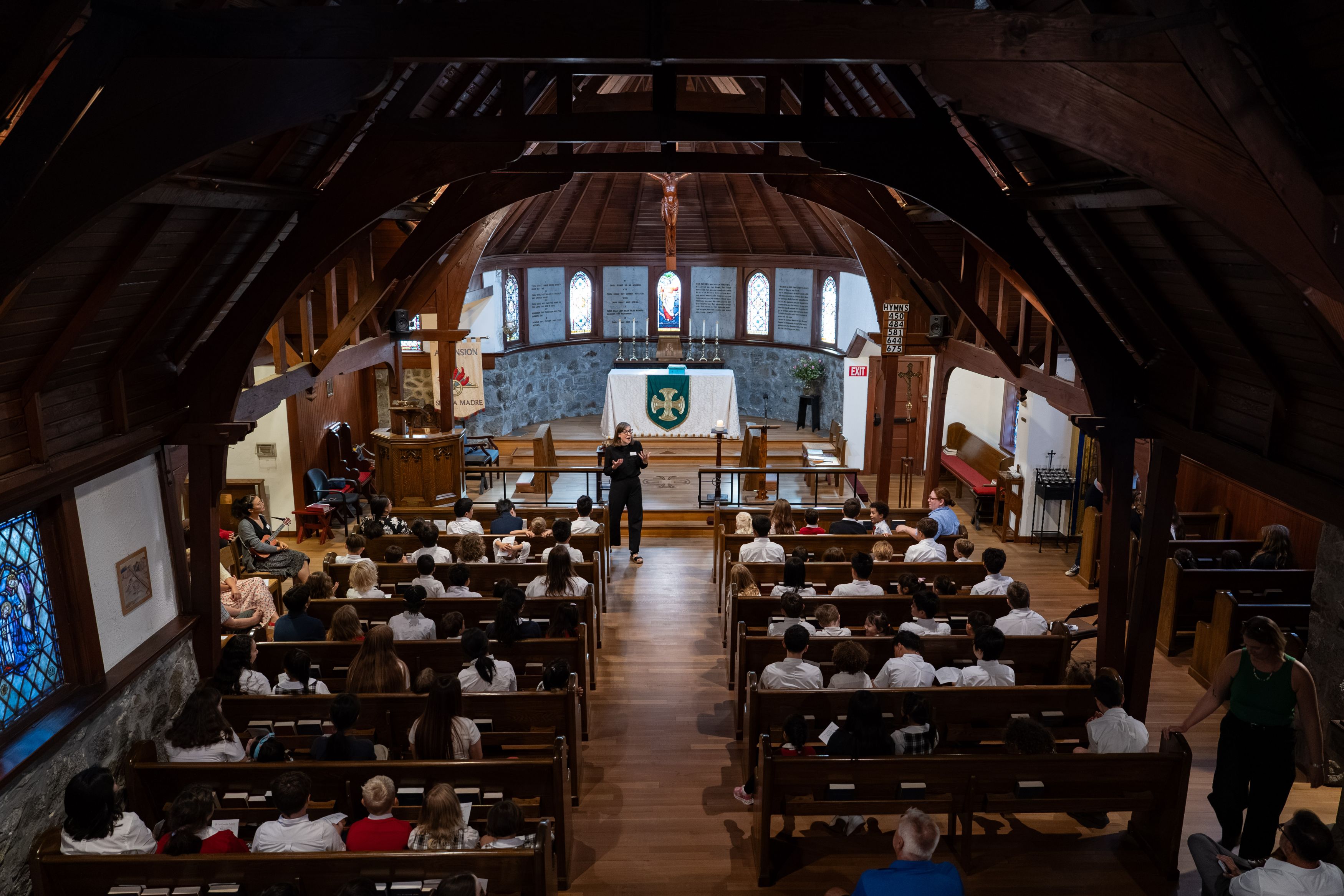 Chaplain Annie addresses a seated audience inside a traditional church sanctuary with wooden pews and a vaulted ceiling.